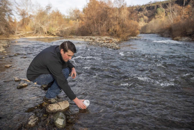 Jackson Webster dips a sampling container into Butte Creek. 