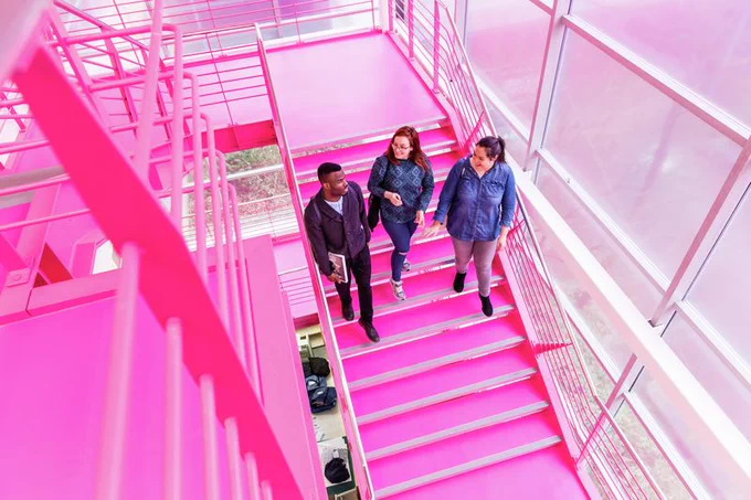 3 students walking down Harrow's pink staircase