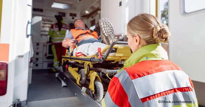 Eine Frau im Rettungsdienst schiebt eine Krankenliege in einen Rettungswagen.