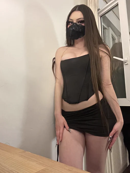 a pic of me in my New Year’s Eve outfit (a black miniskirt and a black corset, i have silver and black press on nails, thigh-length brown hair, brown eyes, eyeliner and dramatic fake eyelashes) wearing a black lace covered N95