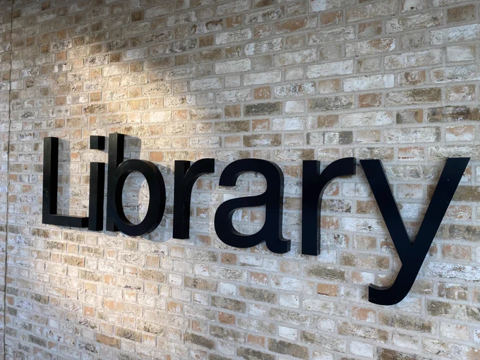 Image shows the exterior ‘Library’ sign against a brick wall