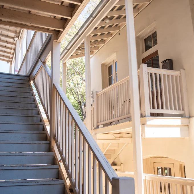 Wooden staircase leading to a balcony with railings at a traditional building, bathed in sunlight.