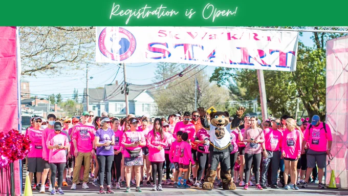 Group of people wearing pink and standing at the start line of a race. Also in the photo is Blades, the Boston Bruins mascot.