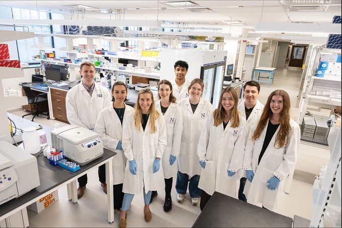Scientists in lab coats smiling in a lab.