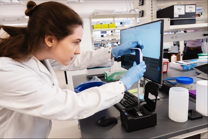 A scientist in a lab coat holding a pipette. 