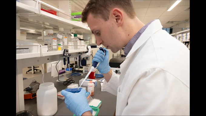 A scientist in a lab coat holding a pipette.