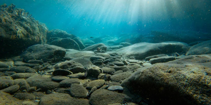 A picture of rocks and stones on the ocean floor, with sunlight filtering through the water over them.