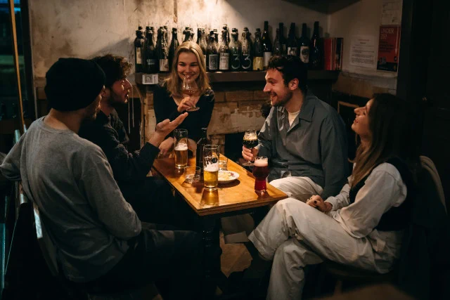 A group of young people socialising around a table drinking pints in a pub.