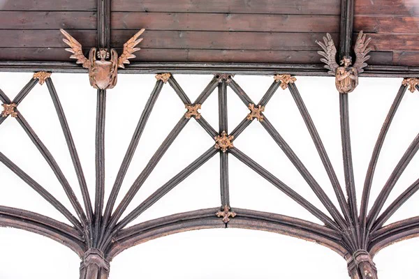 Detail image of the wooden wall-posts, resting upon shield-bearing angel corbels with plaster vaulting and golden foliage bosses beneath. 