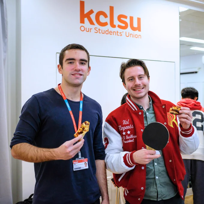 Two men holding pizza and ping pong paddle