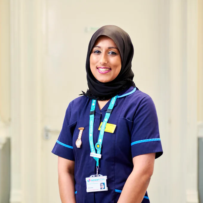 Smiling healthcare professional wearing a hijab and blue scrubs, with a name badge and Dementia UK lanyard.