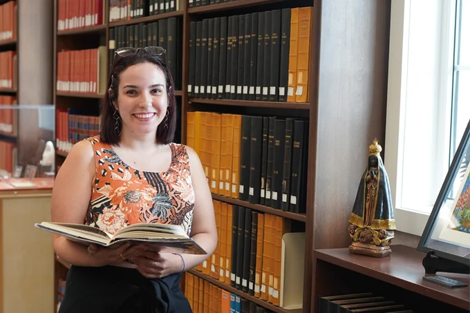 fellow stands in front of bookshelf with an open book and statue of mary on the windowsill