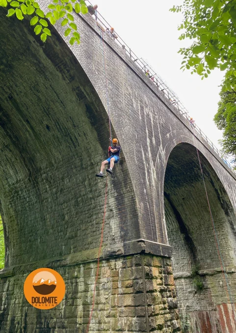 A person abseils down from a bridge. It is a large structure, almost like a viaduct. 