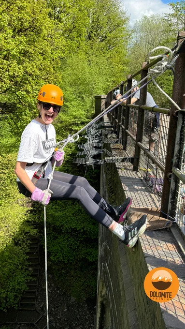 A woman abseils off a bridge surrounded by trees. 