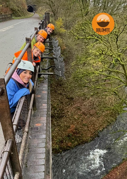 A group of people wearing helmets poke their heads out of fencing at the top of a bridge. 