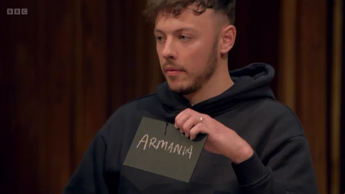 A man holds a chalkboard that reads "Armania", as opposed to "Armani"