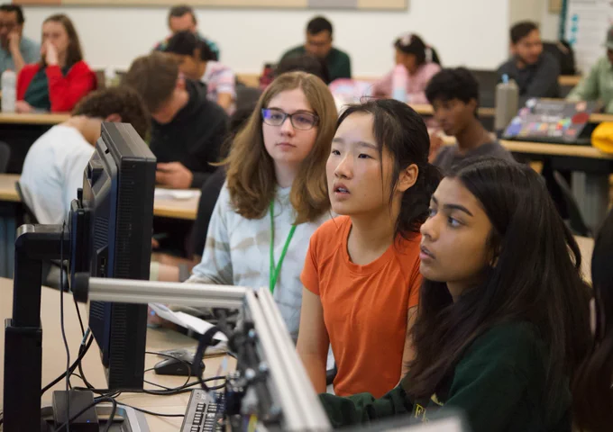 Three students sitting and looking at a computer to the left of the frame
