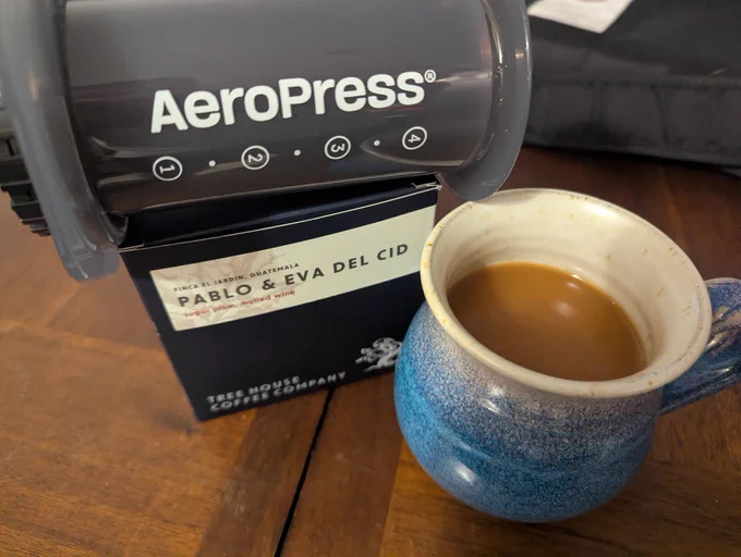 A blue ceramic mug of Treehouse Pablo & Eva  Del Cid coffee made in the aero press. Aero press is laid down sideways on top of the coffee box on the left.