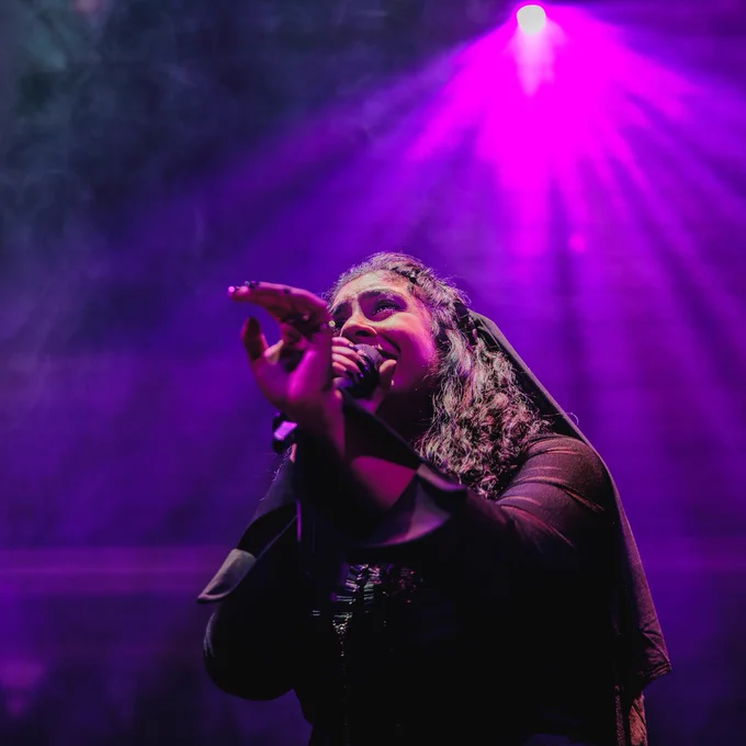 A person performing on stage under purple stage lighting.