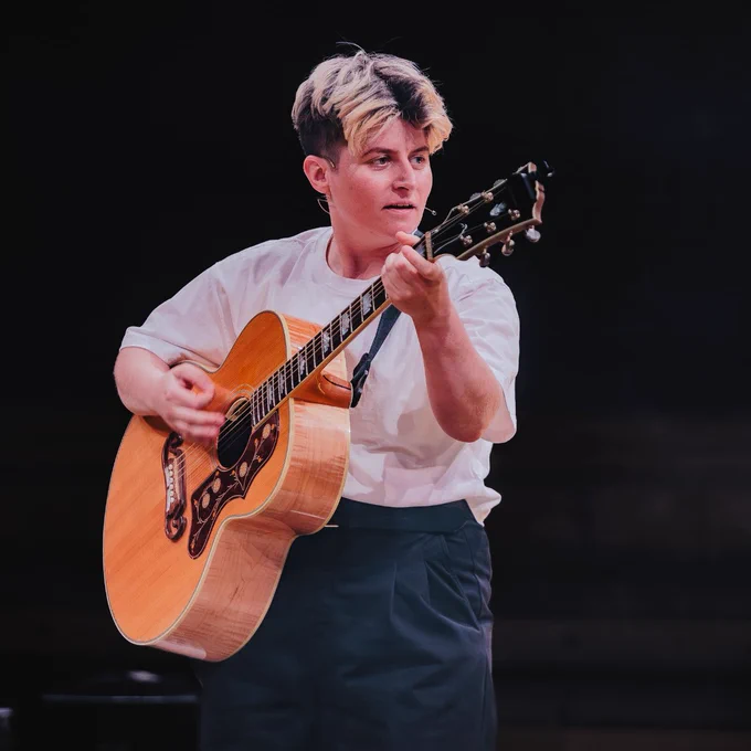 A performer passionately playing an acoustic guitar on stage.