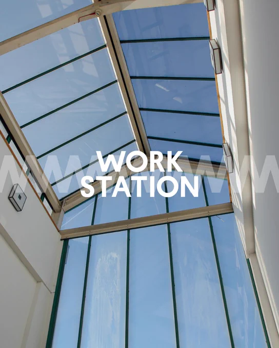 Interior view of a modern workspace featuring a glass ceiling structure allowing ample natural light, with the logo 'WORK STATION' prominently displayed.