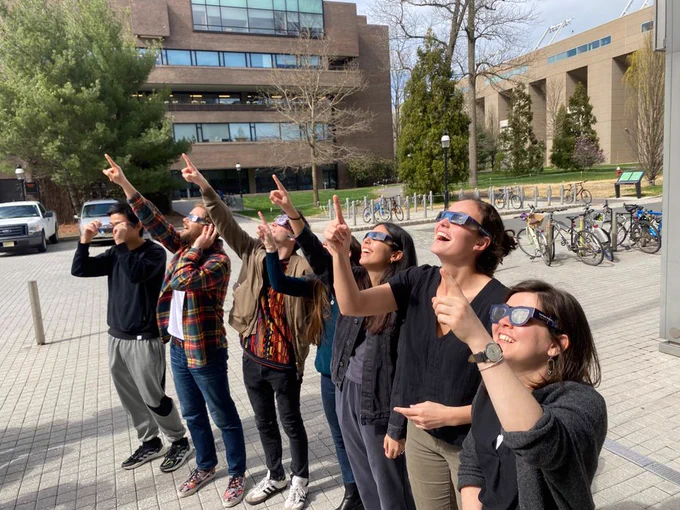 Full-color image of a couple of Weichman Lab members viewing the solar eclipse last summer in front of Frick lab.