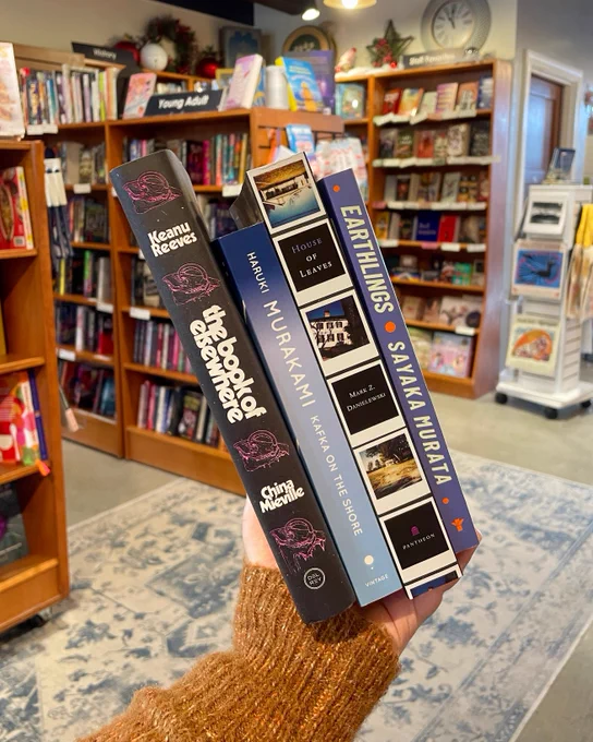 A collection of fiction books held up for the camera. From left to right, they are: The Book of Elsewhere by Keanu Reeves and China Mieville; Kafka on the Shore by Haruki Murakami; House of Leaved by Mark Z. Danielewski; and Earthlings by Sayaka Murata.