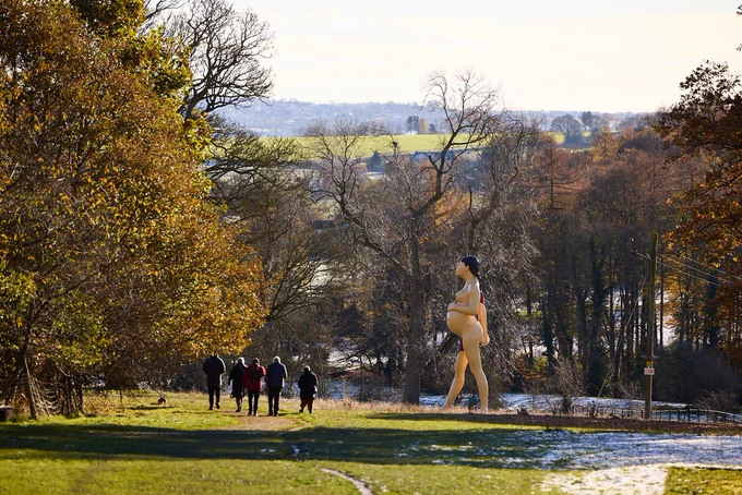 A group of people walking towards a larger-than-lifesize sculpture of a pregnant woman outdoors.