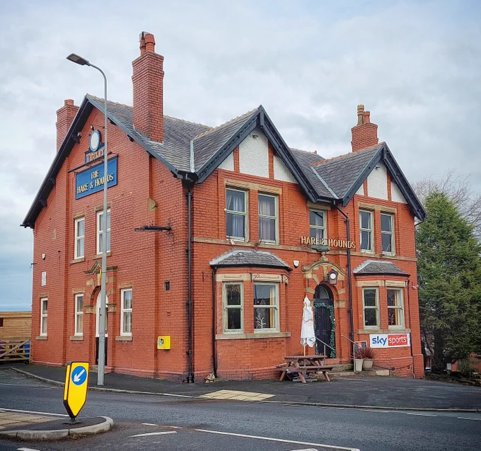 A colour photo of a large, detached redbrick pub, with 'Hare & Hounds' above the door, and 'Thwaites...The Hare & Hounds' on the side.