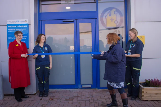 A staff member cuts a blue ribbon held by three other members of the Sheffield Children’s team in front of the blue front door of Embrace’s new premises