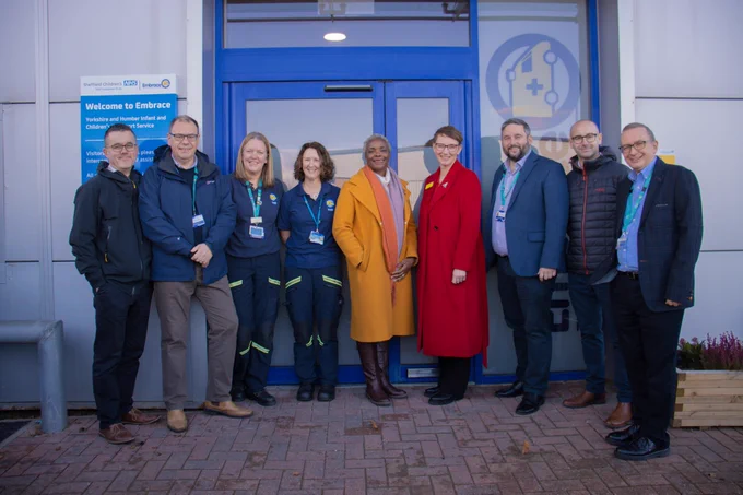 A group of Sheffield children’s staff members, including members of the executive and embrace teams, smile outside of the blue front door of the new premises.