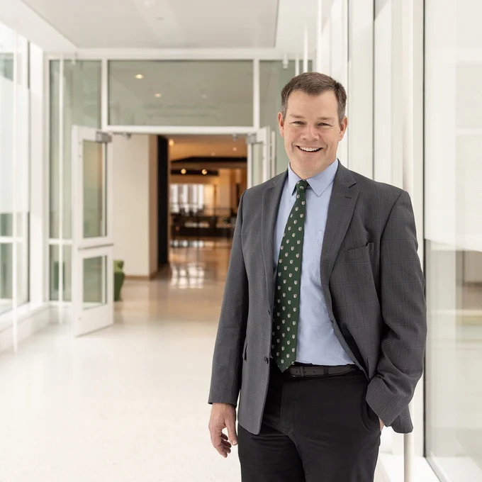 Thayer School of Engineering at Dartmouth's Interim Dean Douglas Van Citters is standing and smiling in a dark gray suit, blue shirt, and green tie on the Opus Foundation Bridge in Class of 1982 Engineering and Computer Science Center.