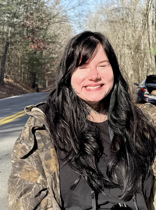 A photo of poetry contest winner Rachel Stempel, standing on the side of a road lined with trees. 