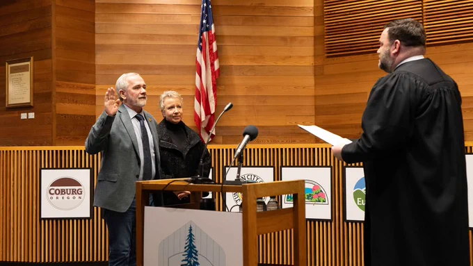 Commissioner Pat Farr, accompanied by his wife Debi, raises his right hand and takes the oath of office from Presiding Judge Jay McAlpin. A U.S. flag is visible in the background.