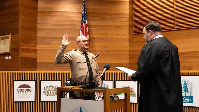 Sheriff Cliff Harrold raises his right hand and takes the oath of office from Presiding Judge Jay McAlpin. A U.S. flag is visible in the background.