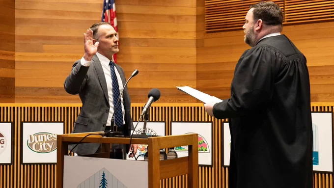District Attorney Chris Parosa raises his right hand and takes the oath of office from Presiding Judge Jay McAlpin. A U.S. flag is visible in the background.