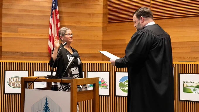 Commissioner Laurie Trieger raises her right hand and takes the oath of office from Presiding Judge Jay McAlpin. A U.S. flag is visible in the background.