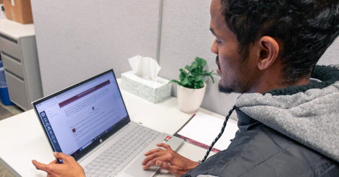 Person sitting at a desk using a laptop with documents open on the screen.