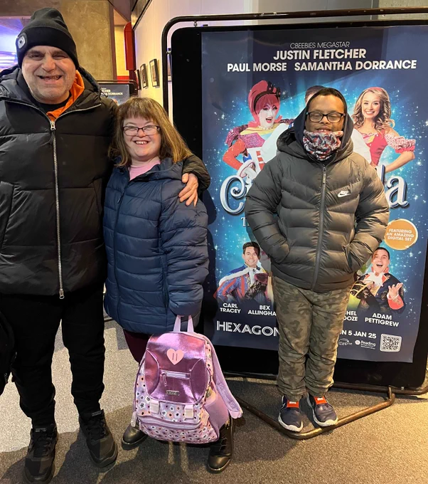 Two men and a woman wearing winter coats are standing in front of a big sign advertising Cinderella at the Hexagon.