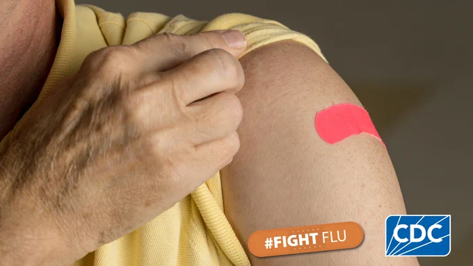 A person's arm with a red bandage. The CDC logo and an orange bandage with the hashtag #FightFlu are overlaid in the bottom right corner.