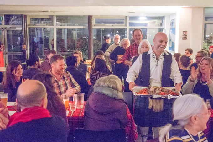 The MC carries the haggis though the tables of guests in a ceremonial display, with musicians playing their instruments in a line behind him.