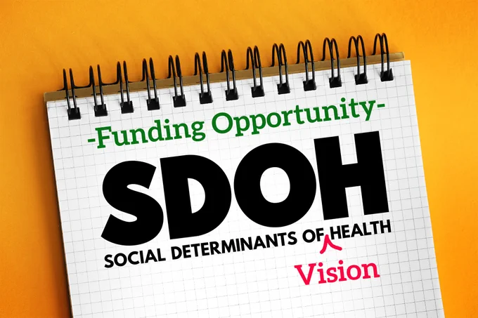 A spiral notebook with the words "Funding Opportunity: SDOH Social Determinants of Vision Health" written on a page, set against an orange background. Adapted from Adobe Stock