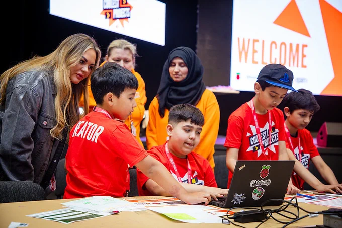 A group of young creators in red t shirts looking at a laptop with their mentors.