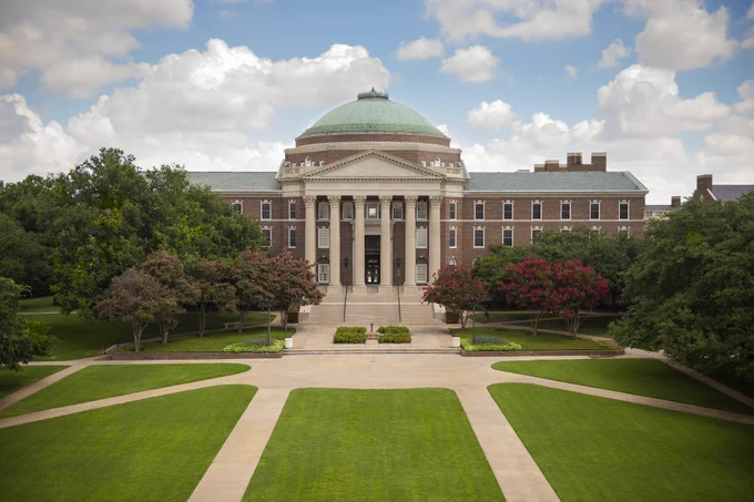 View of the iconic Dallas Hall at Southern Methodist University, featuring its distinguished dome and classical architecture, surrounded by manicured lawns and lush, flowering shrubs.