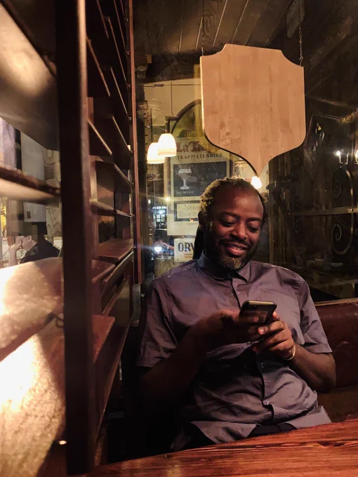 Kwame Phillips sat at a table in bar smiling and looking down at a smart phone