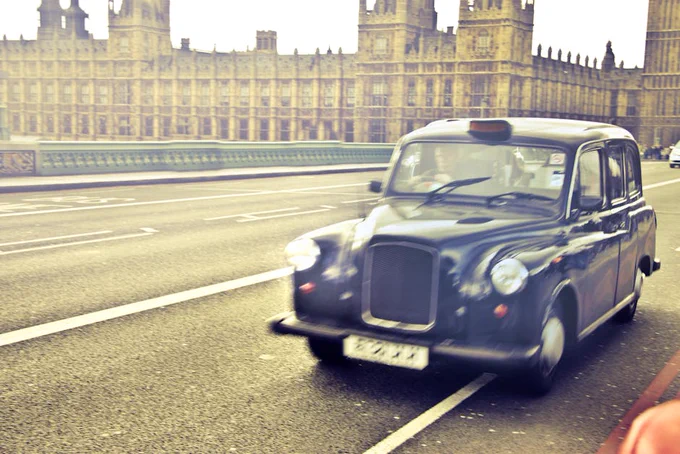 Classic London taxi speeding past the Houses of Parliament in a vibrant urban scene.