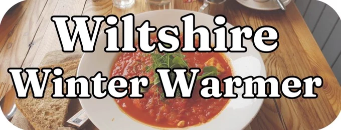 The image appears to depict a bowl of tomato-based soup or stew, garnished with greens, served on a wooden table with a slice of brown bread on the side. The text overlay reads: "Wiltshire Winter Warmer". The theme suggests a cosy, hearty dish ideal for colder months, potentially promoting a local or seasonal dining experience.

