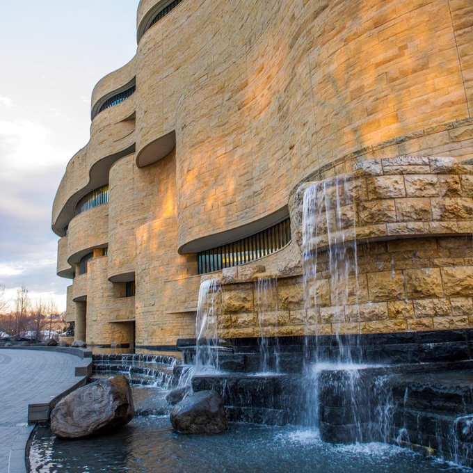Exterior view of the National Museum of the American Indian featuring its unique curvilinear architecture and a cascading waterfall at the entrance.