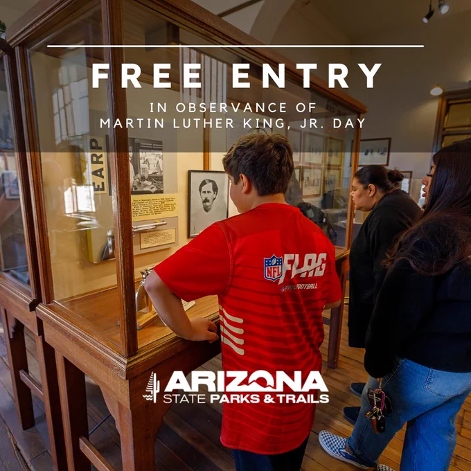 Visitors observing exhibits at an Arizona State Parks & Trails museum on Martin Luther King, Jr. Day, which offers free entry as advertised on the informational poster.
