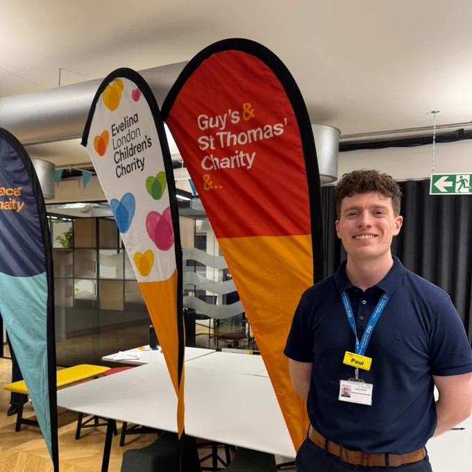 Paul standing in front of Guy's and St Thomas' Charity, Evelina London Children's Charity and Guy's Cancer Charity banners.